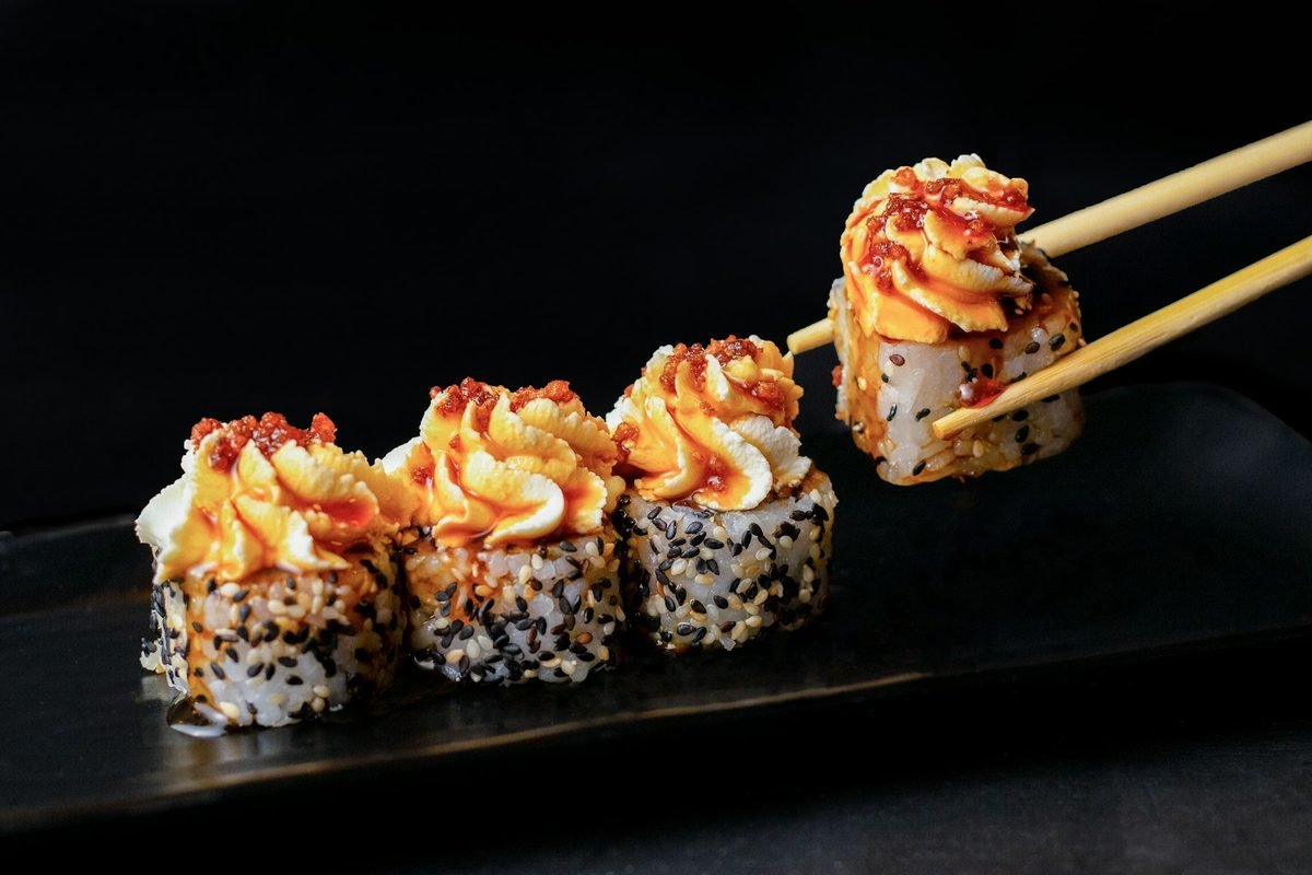Chopsticks lifting a sushi roll topped with spicy sauce